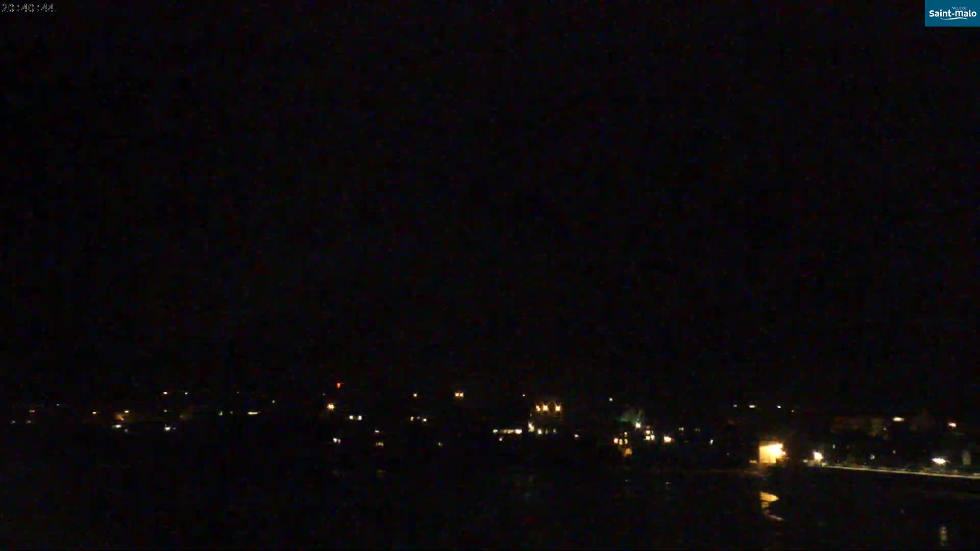 A nighttime long shot shows a dark, mostly obscured town with faint lights visible against a black sky.