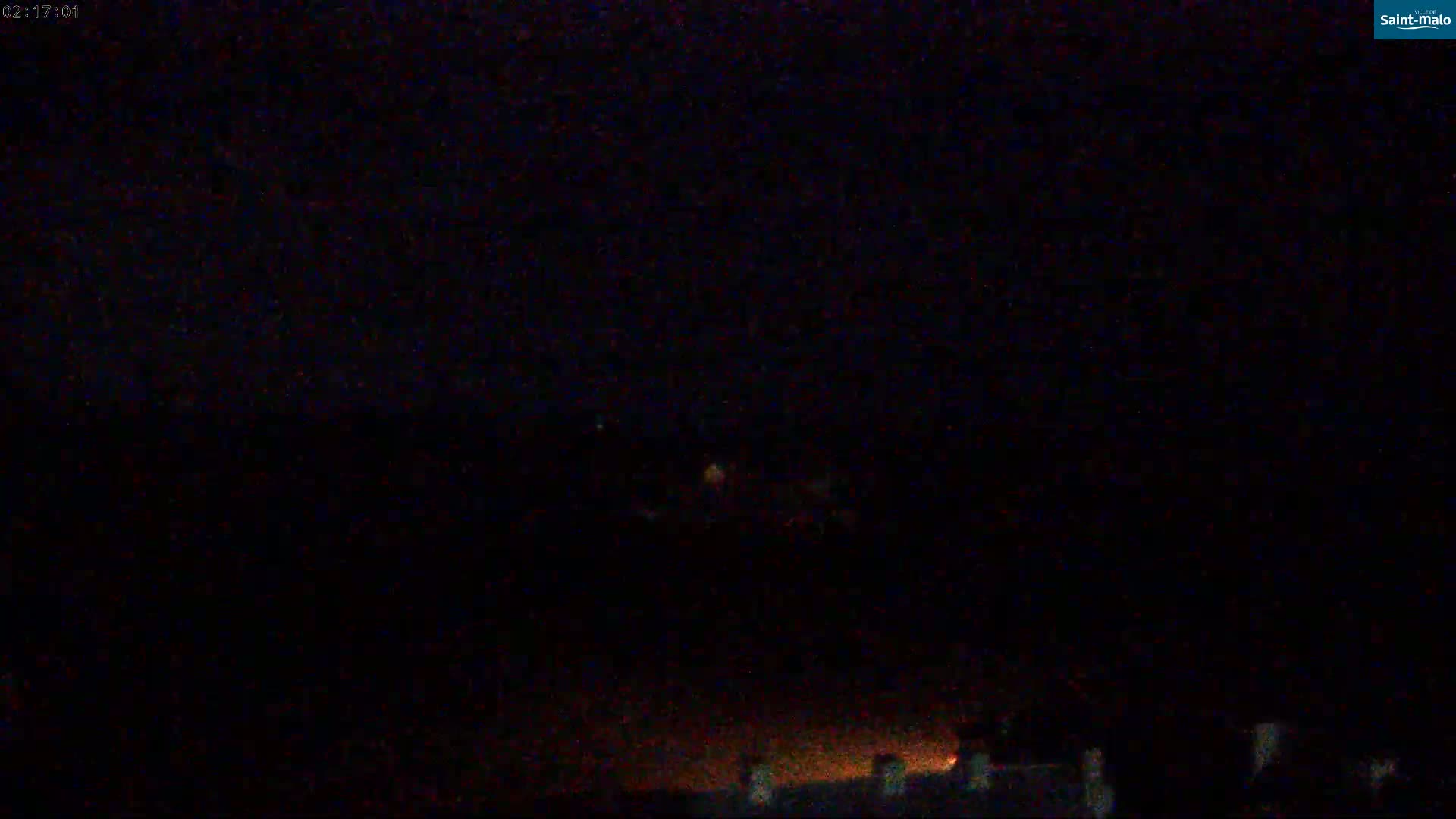 A dark, nighttime scene shows a few faint lights on the horizon.