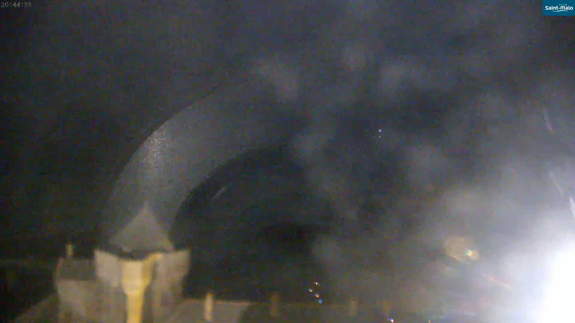 A dark, blurry image shows a large, dark object, possibly a vehicle, at night with hazy or foggy conditions.