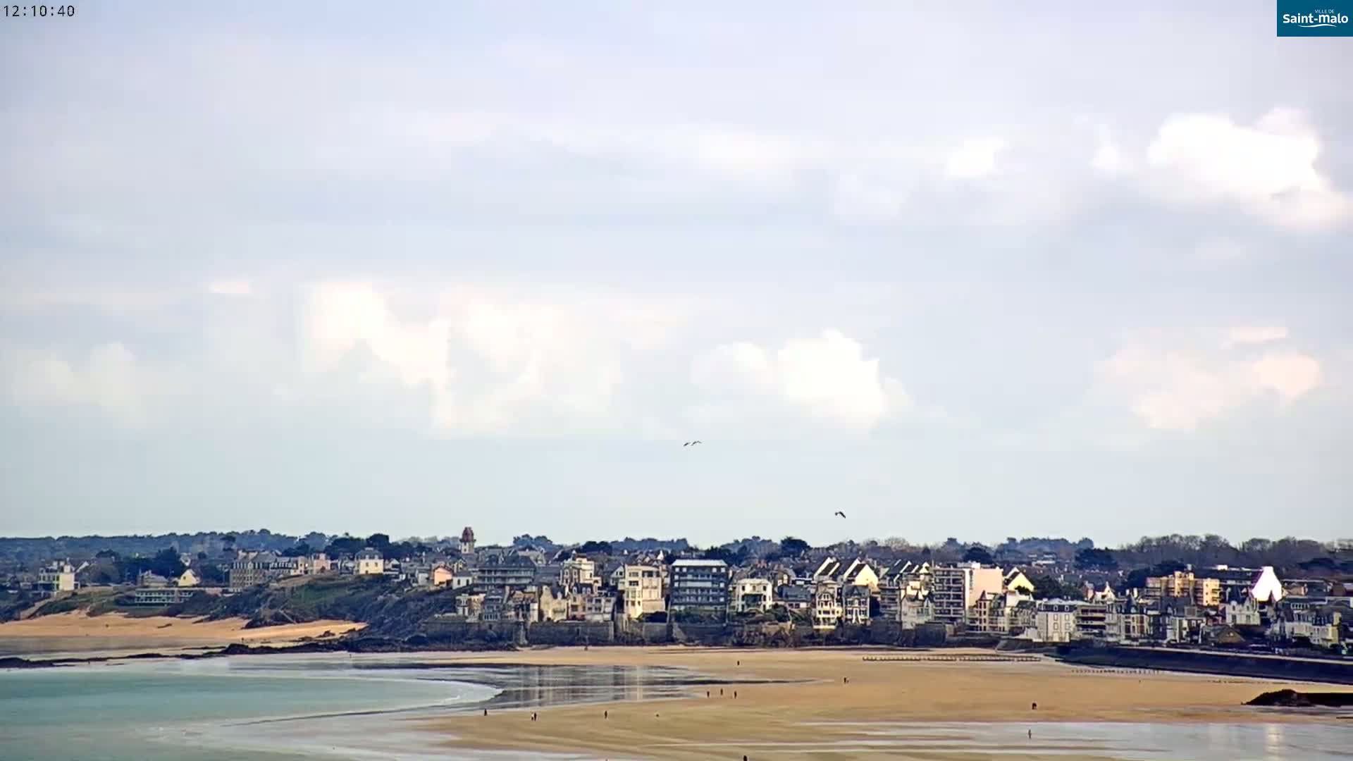 A coastal town with buildings along a sandy beach is visible under a partly cloudy sky.