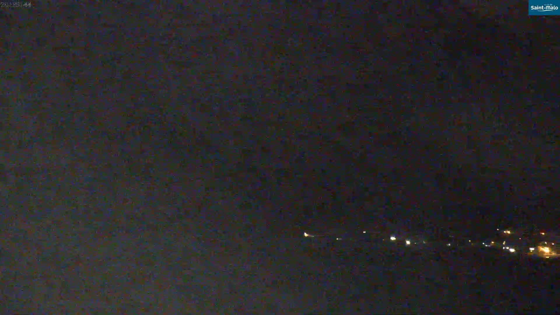 A nighttime long shot shows a dark, possibly cloudy sky over a distant line of faint lights.