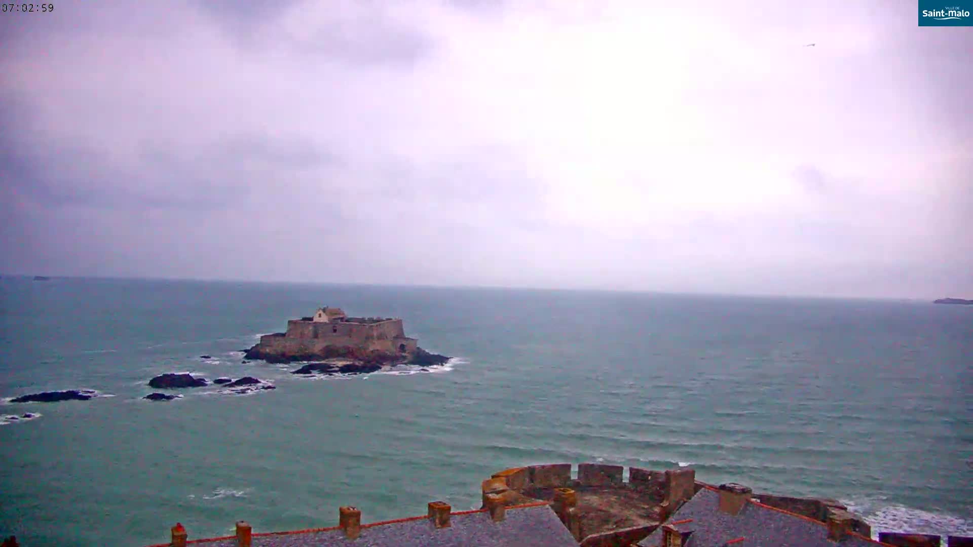 A stone fortress sits on a rocky island in a calm, gray sea under an overcast sky.