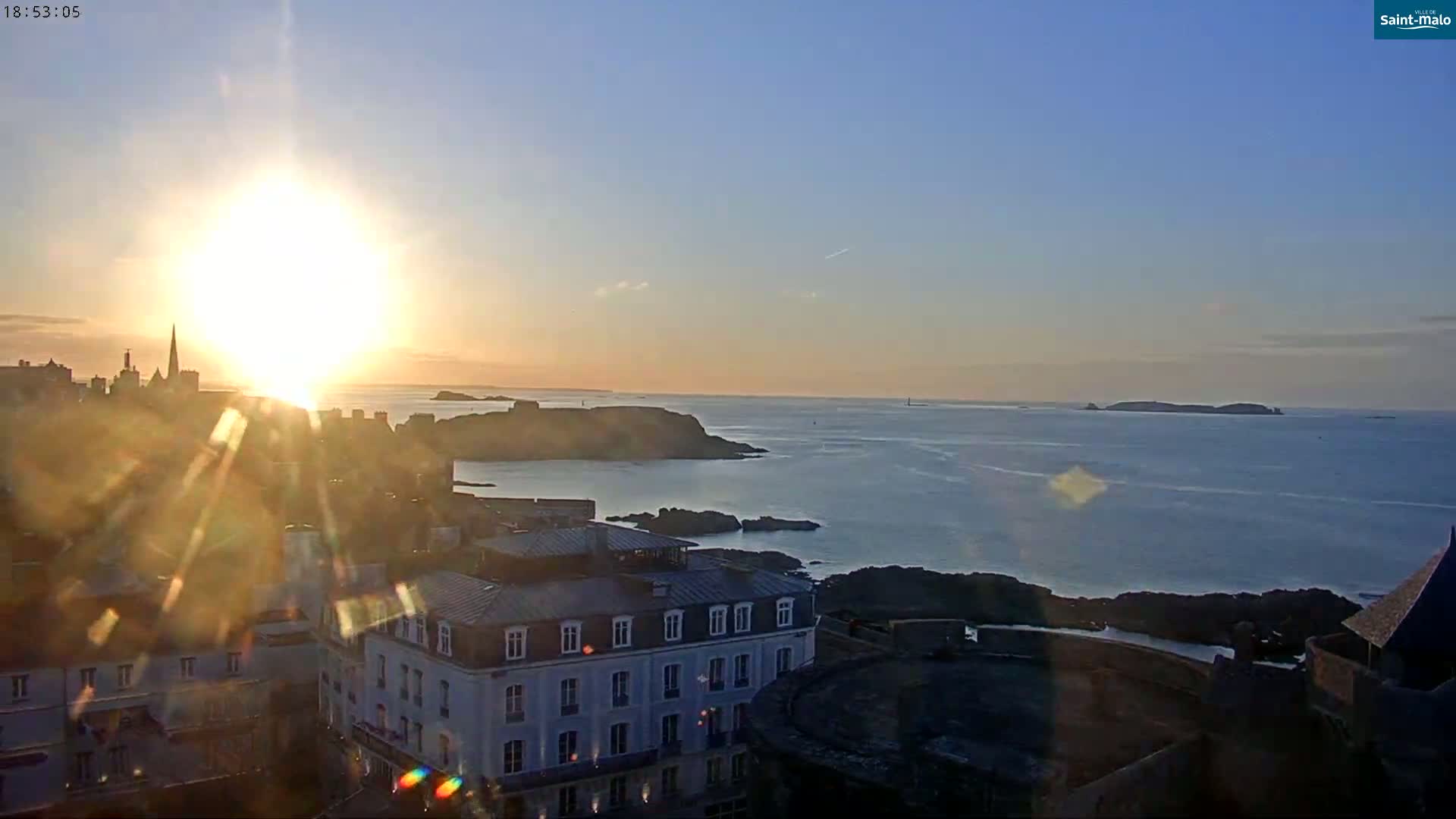 A coastal city is seen at sunset over a calm ocean with islands in the distance.