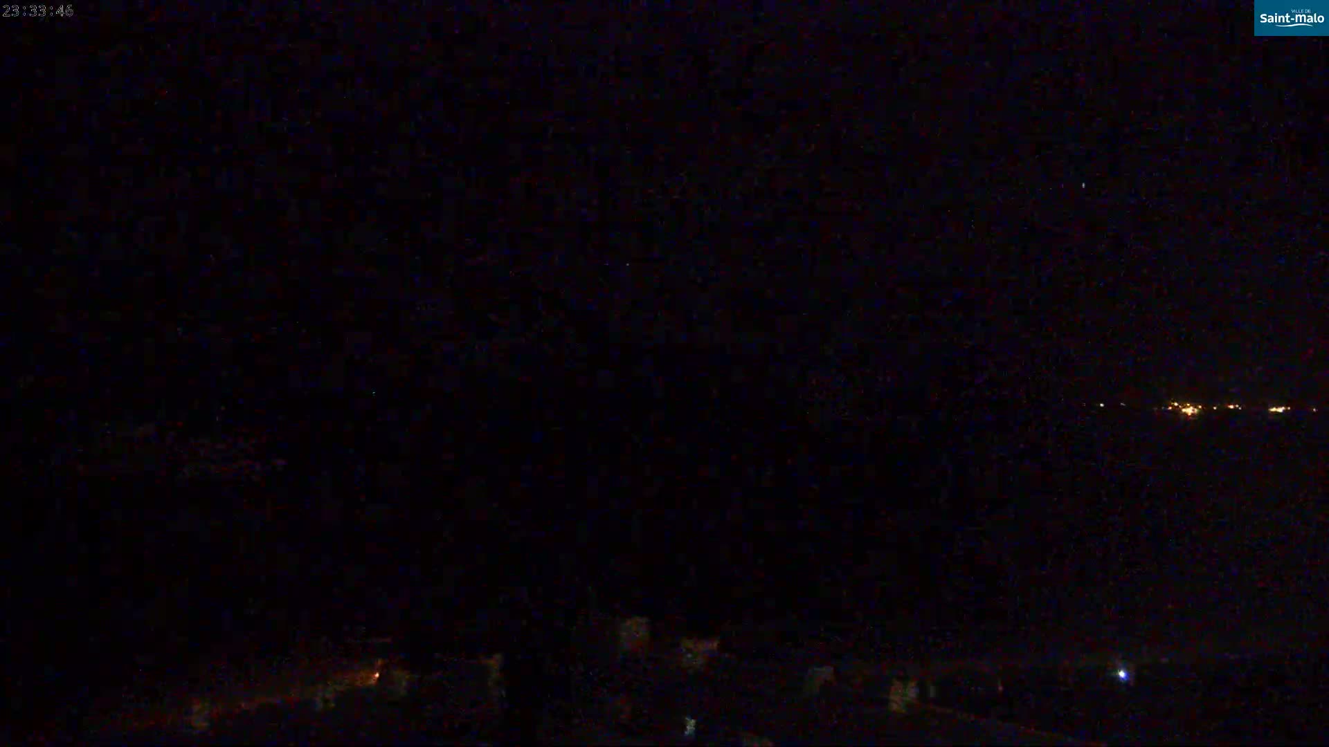 A nighttime view shows a dark landscape with a distant line of lights under a clear, dark sky.