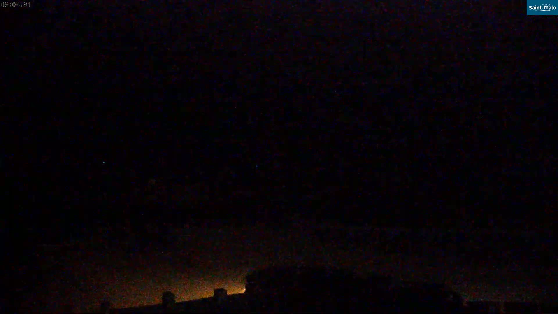 A nighttime outdoor scene shows a dark sky with a few faint lights on the horizon, likely city lights.