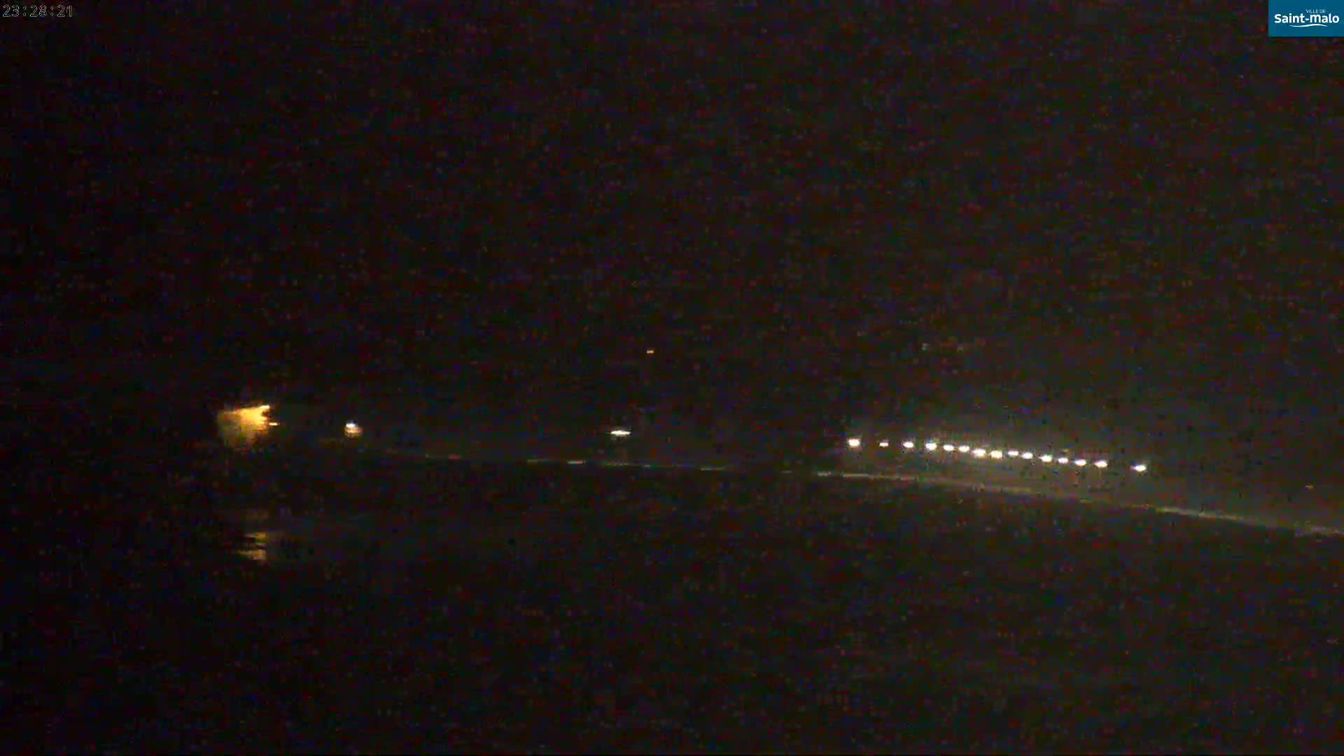 A nighttime, low-light image shows a dark landscape with a line of distant lights, possibly vehicles, on a road or shoreline.