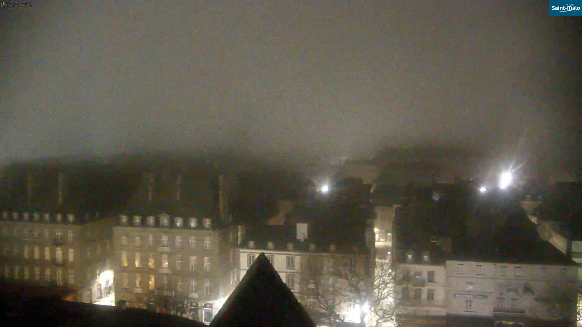 A foggy night scene shows a city with multiple buildings illuminated by streetlights.