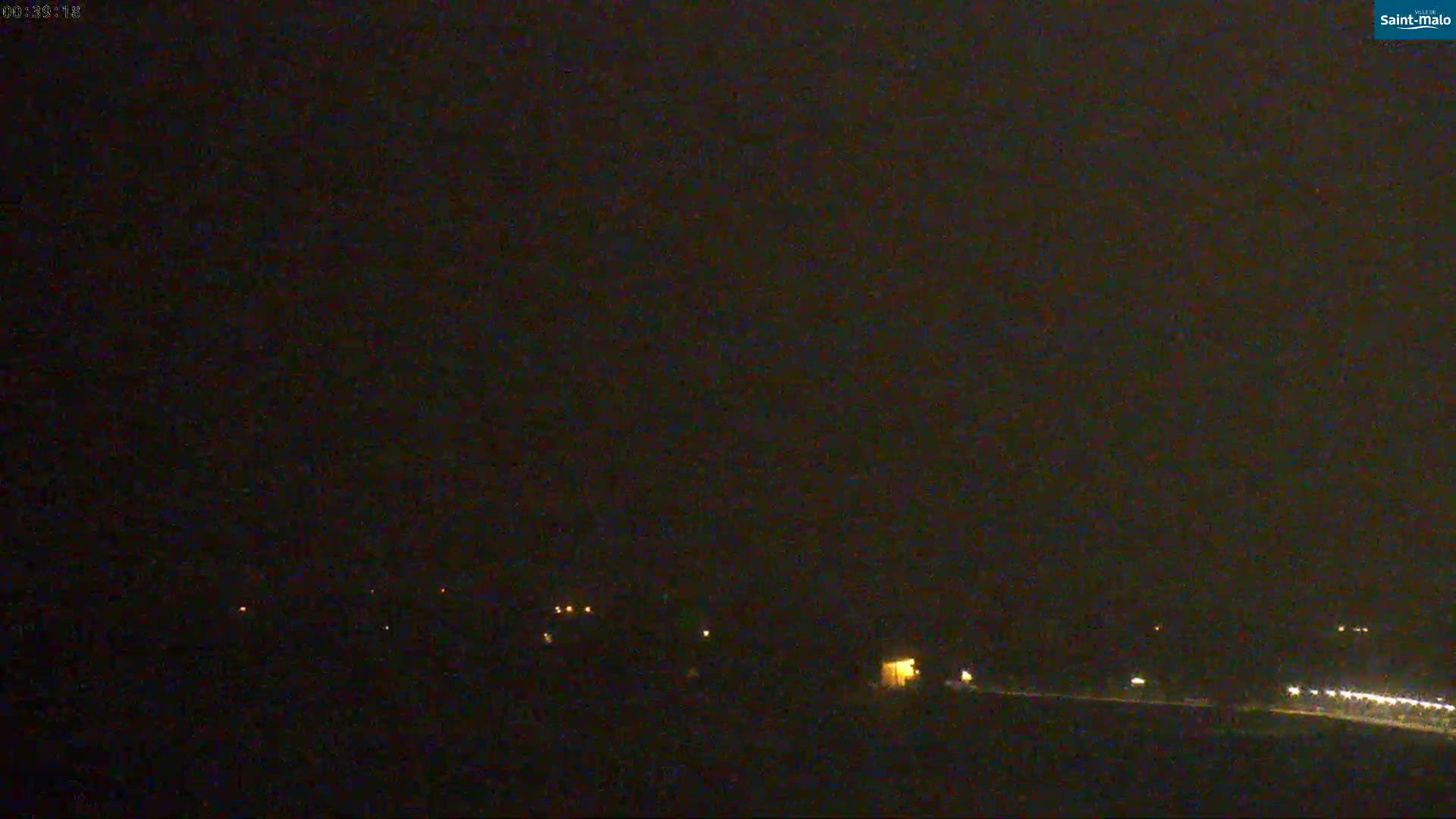 A nighttime, dark scene shows a few distant, faint lights on the ground.