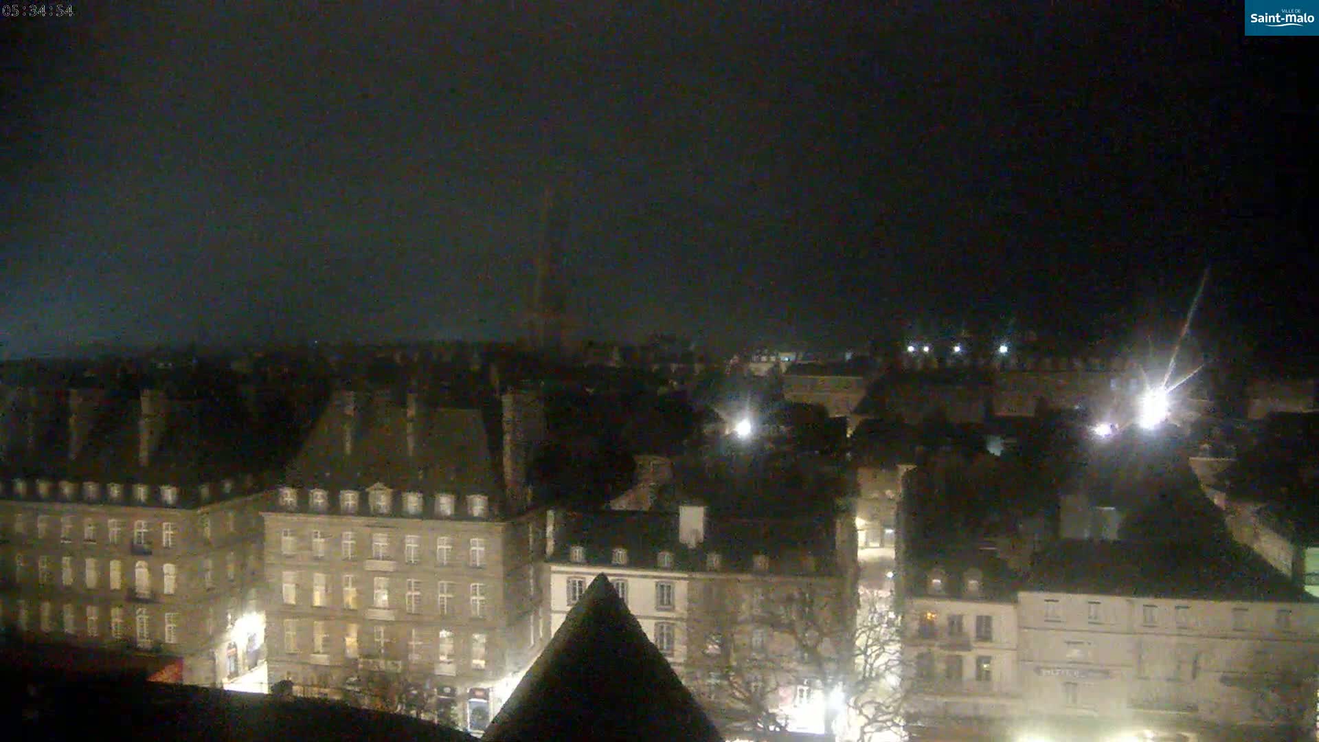 A nighttime, high-angle view of a city's rooftops and buildings under a dark, clear sky.