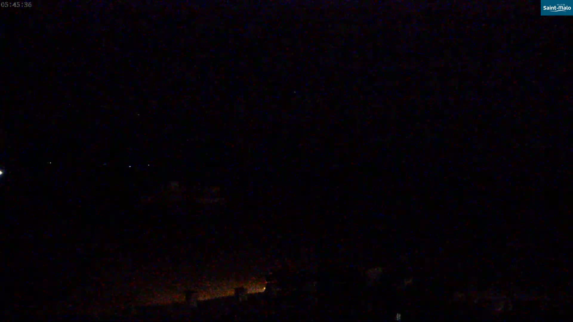 A nighttime, low-light view of a dark sky with a few visible stars and faint lights on the ground below.
