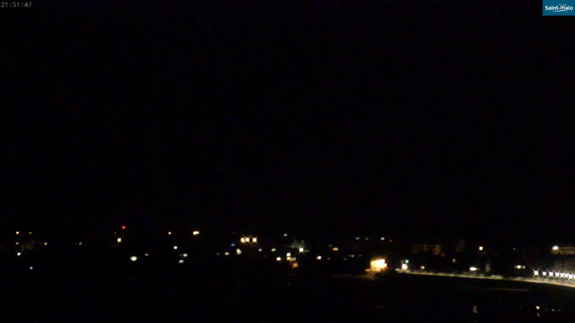 A dark, nighttime view of a distant town or city with scattered lights visible under a clear, black sky.