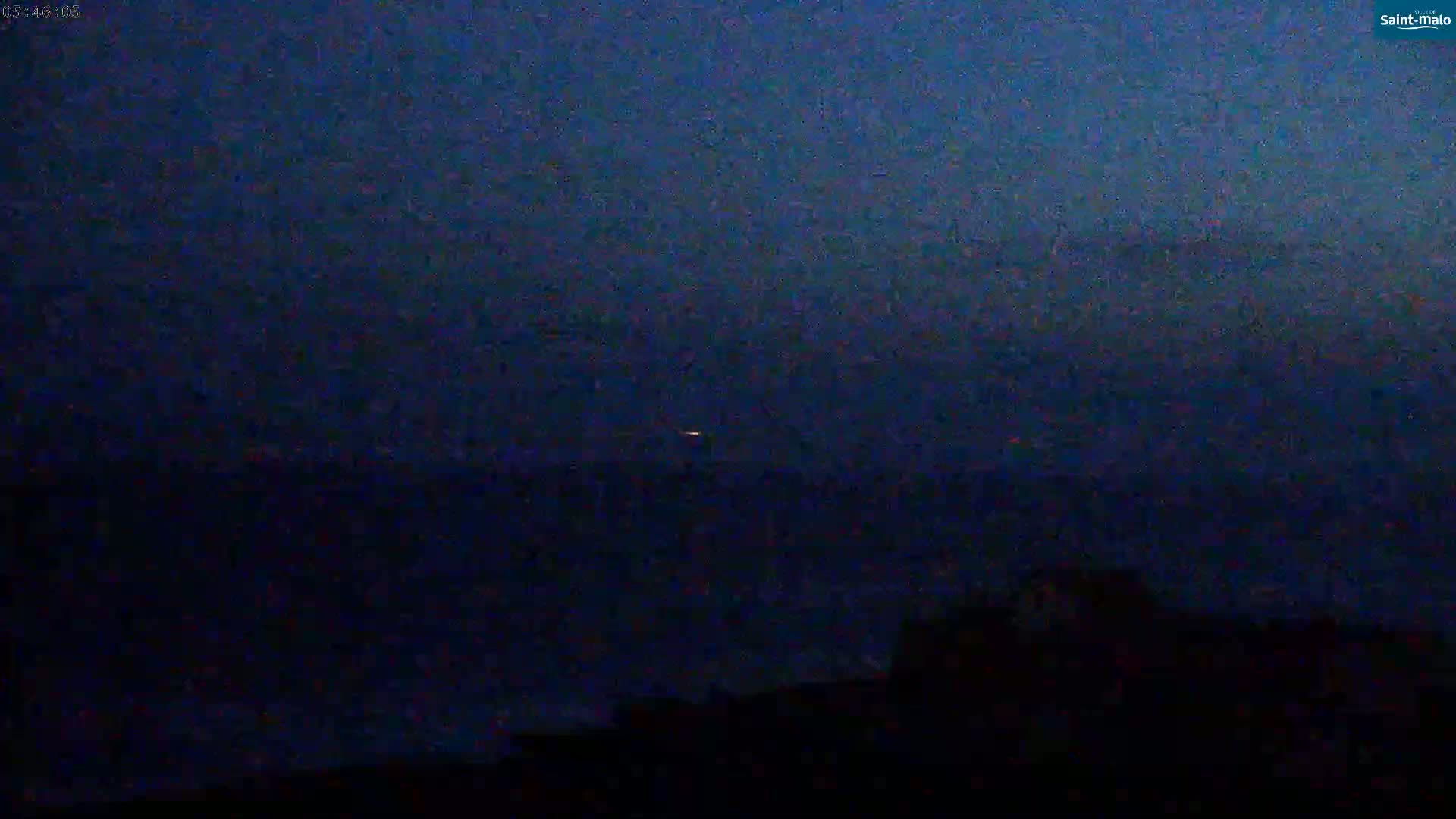 A dark, nighttime scene shows a distant, faint light over a dark body of water with a dark, silhouetted landmass in the foreground.
