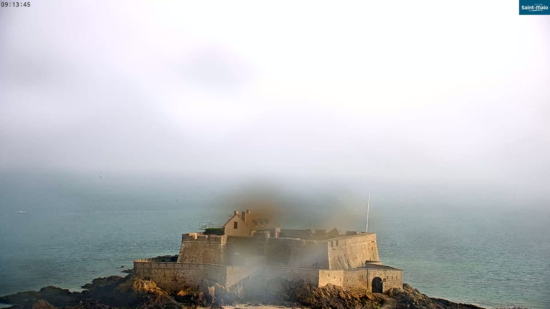 A stone fortress sits on a rocky outcrop surrounded by a foggy sea.