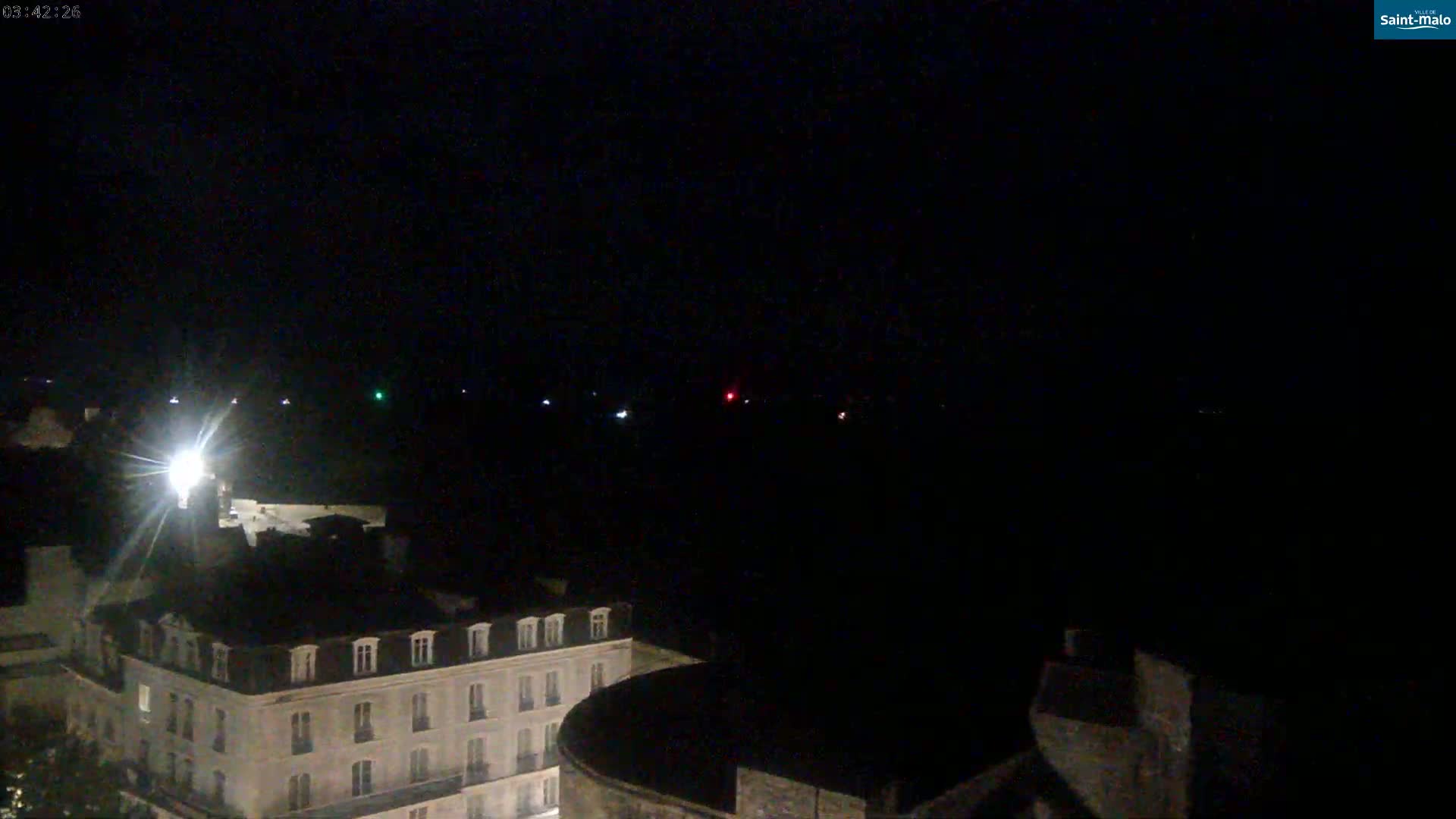 A nighttime view shows a multi-story building and a distant, dimly lit horizon with a few scattered lights.