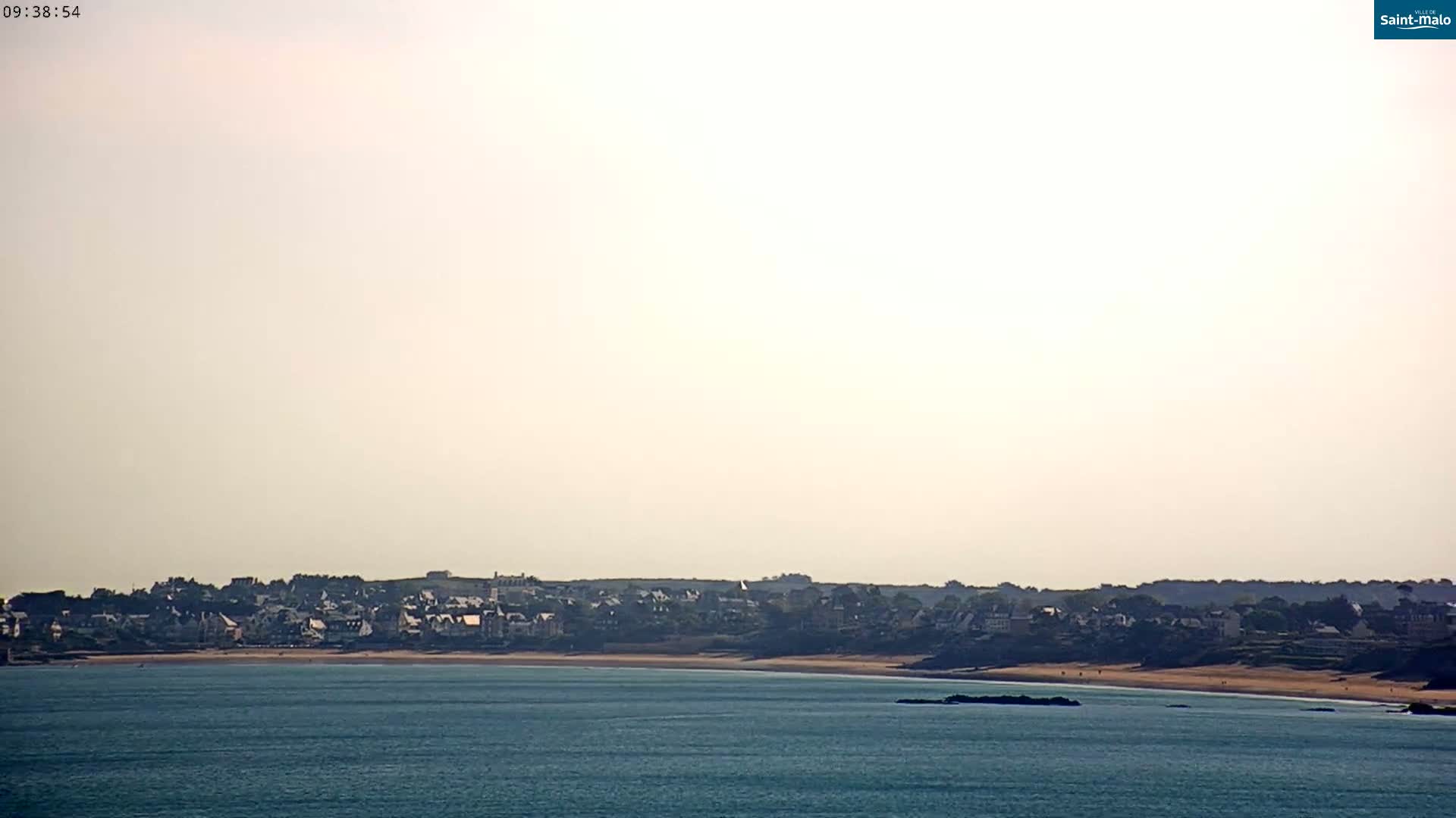 A hazy coastal town with a sandy beach is visible across a calm body of water.