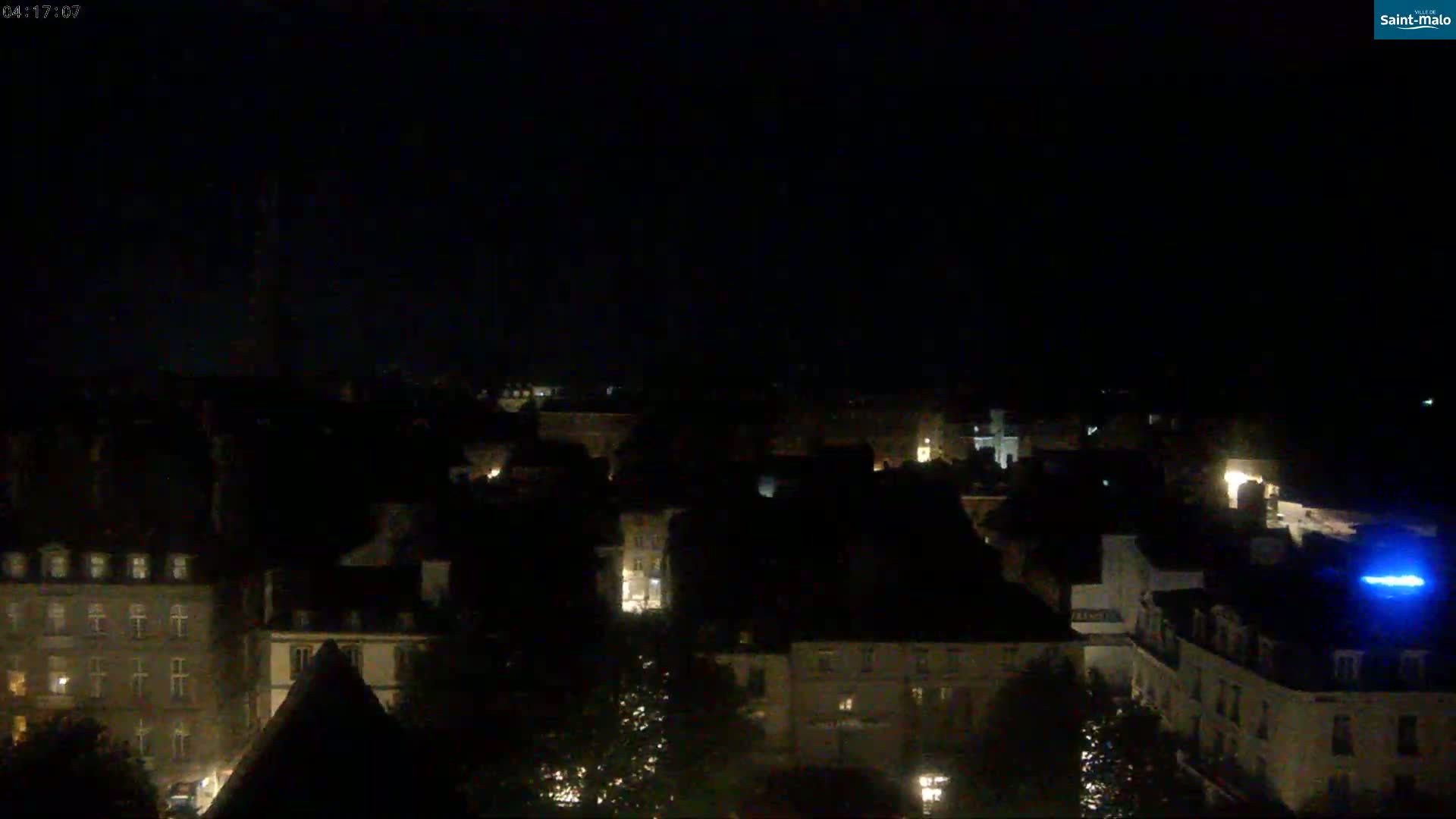 A nighttime, high-angle view of a city with dimly lit buildings under a dark sky.