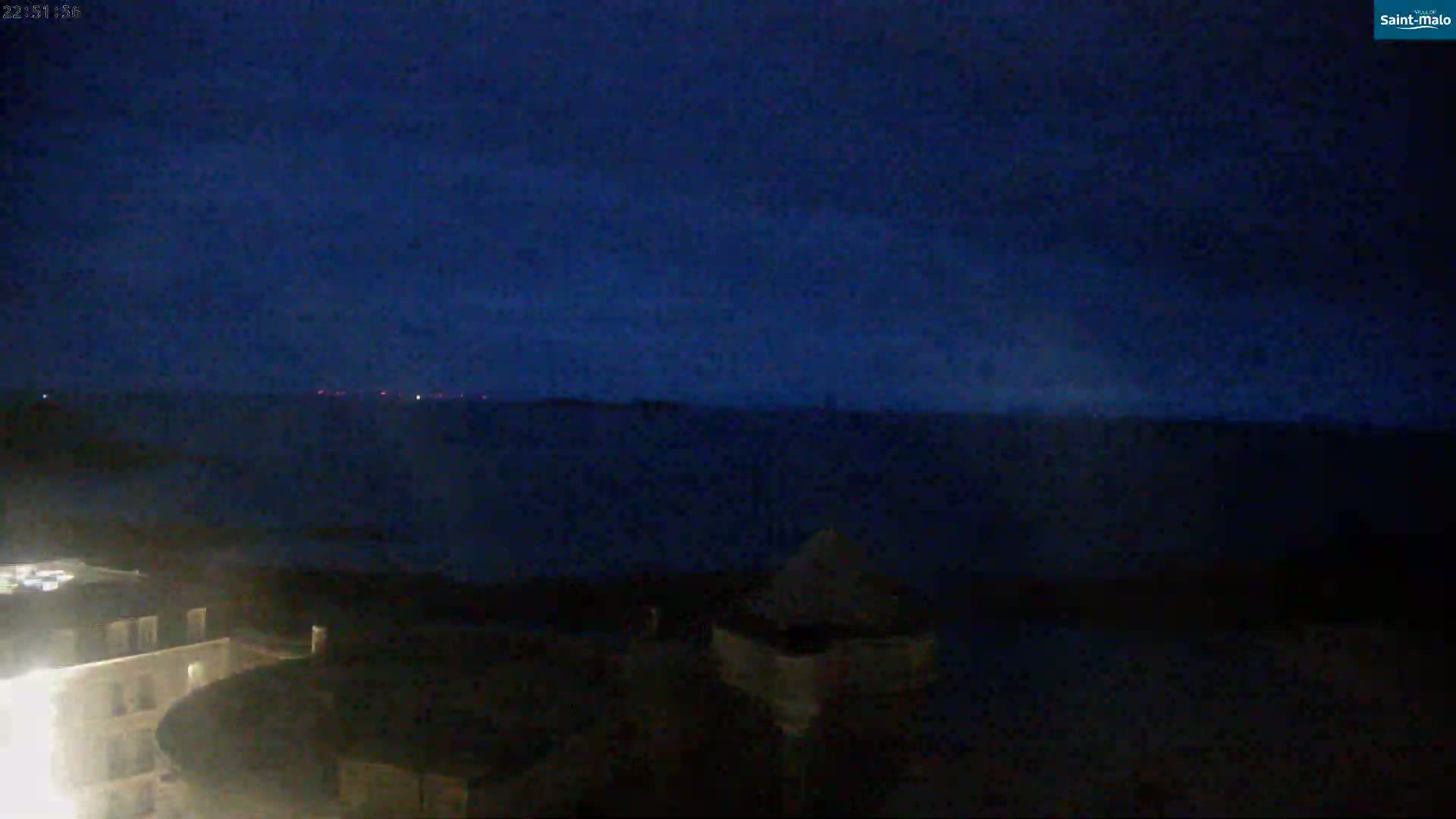 A dark, nighttime view of a body of water under a mostly clear, dark blue sky, with dimly lit structures visible in the foreground.