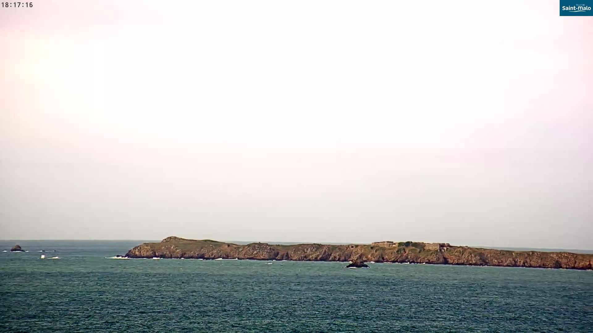 A long, low-lying rocky island is visible on the horizon over a calm sea under a pale, overcast sky.