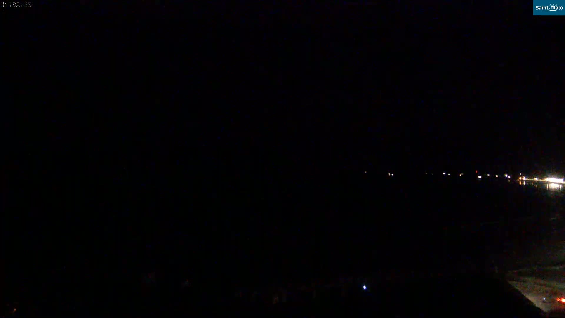 A dark, nighttime scene shows a body of water with a few faint lights visible in the distance.