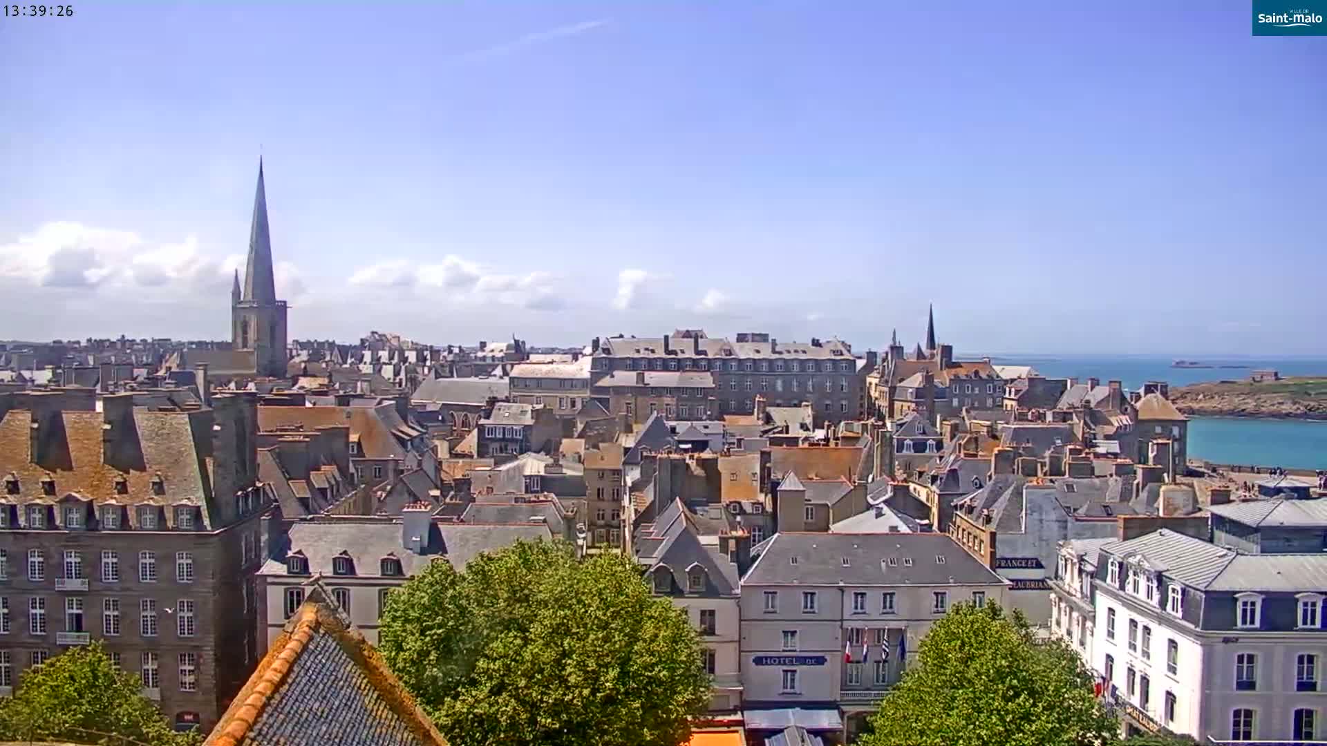 A coastal town with numerous grey-roofed buildings and a tall church spire is visible under a mostly sunny sky.