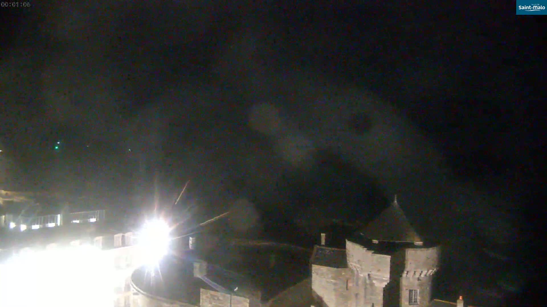 A nighttime long shot shows a stone structure, possibly a castle, under a dark, cloudy sky.