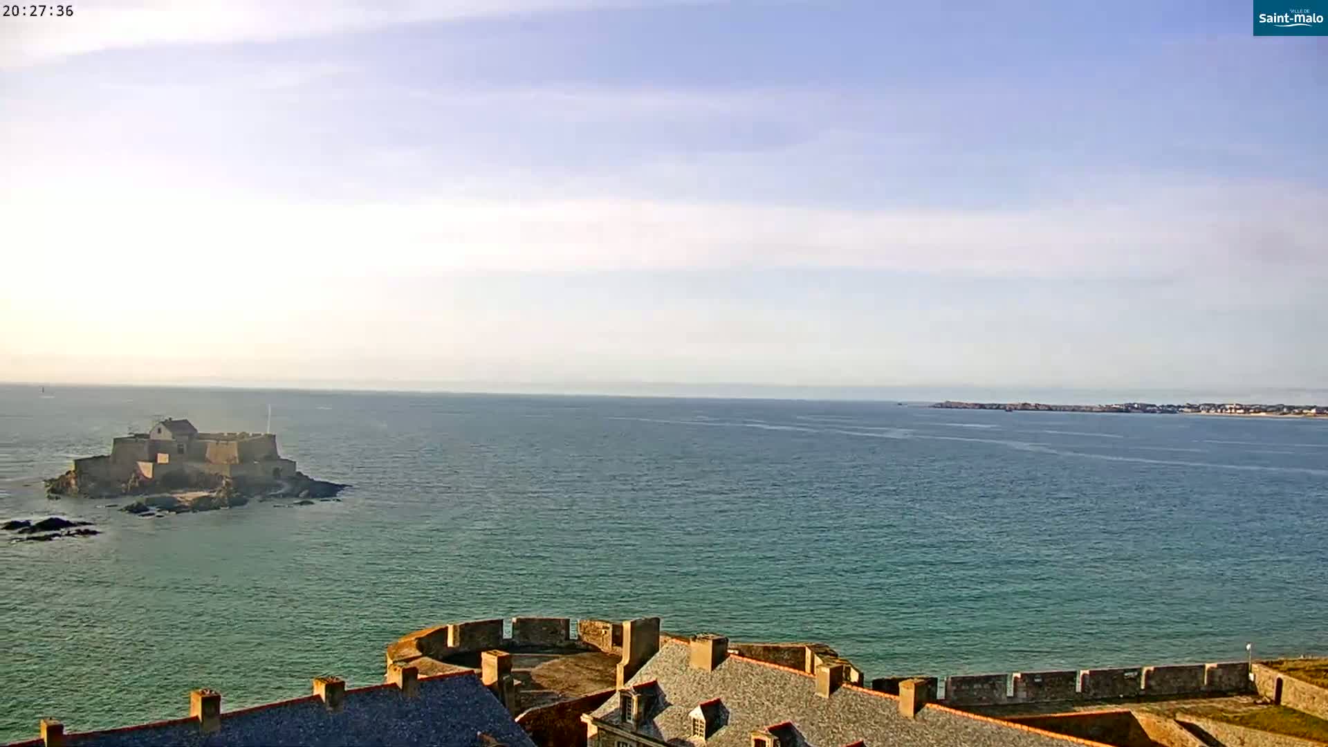 A coastal fortress overlooks a calm sea, with a smaller island fortress visible in the distance under a clear sky.