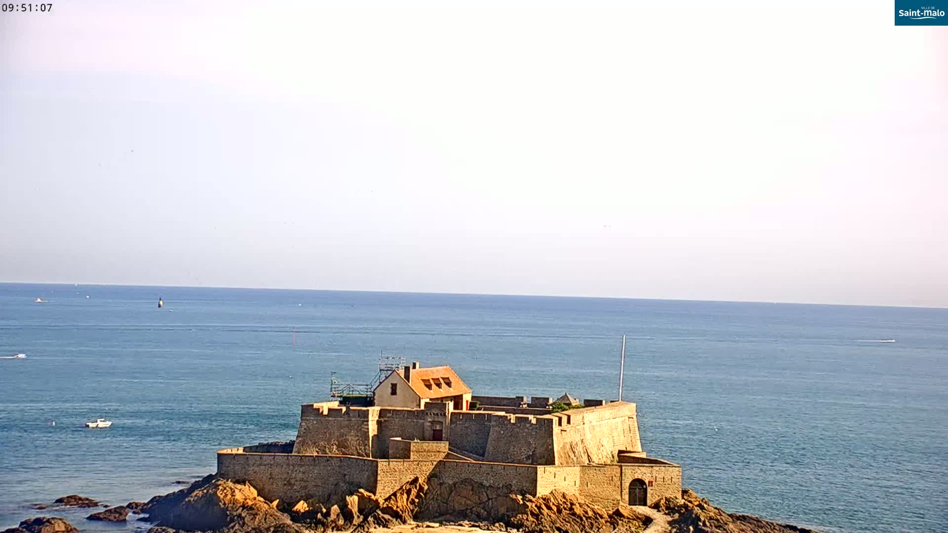 A stone fort sits on a rocky outcrop in a calm sea under a clear sky.