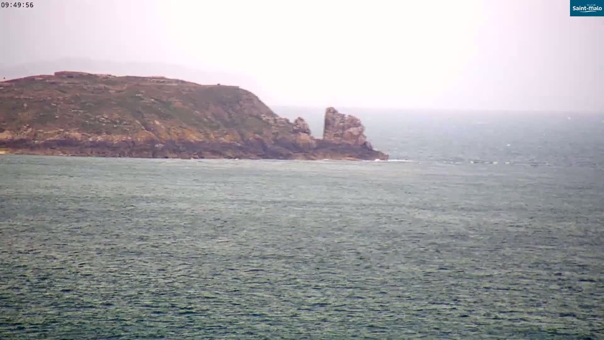 A rocky, grassy headland juts into a choppy sea under an overcast sky.