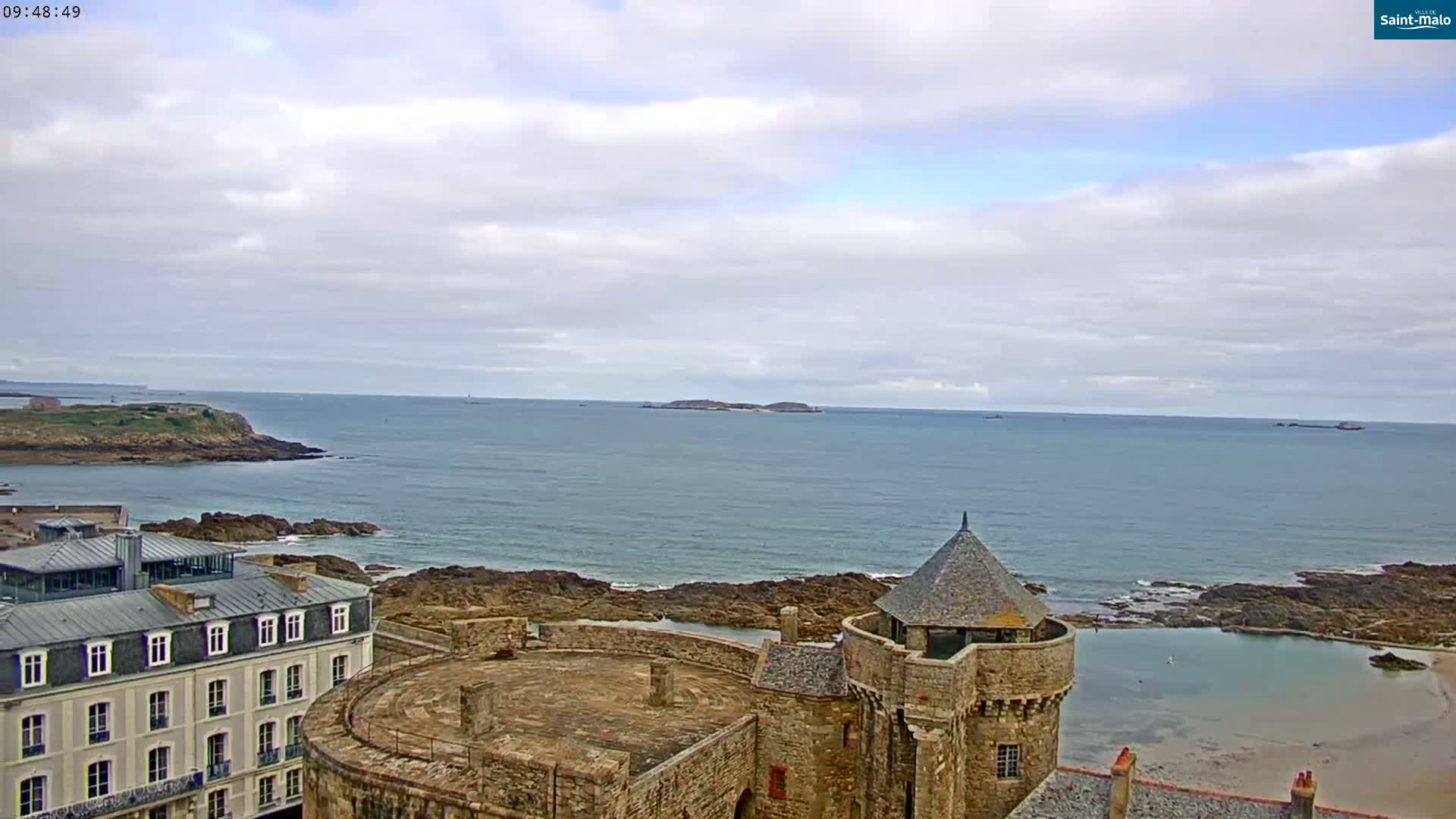 A stone castle overlooks a calm ocean under a cloudy sky.