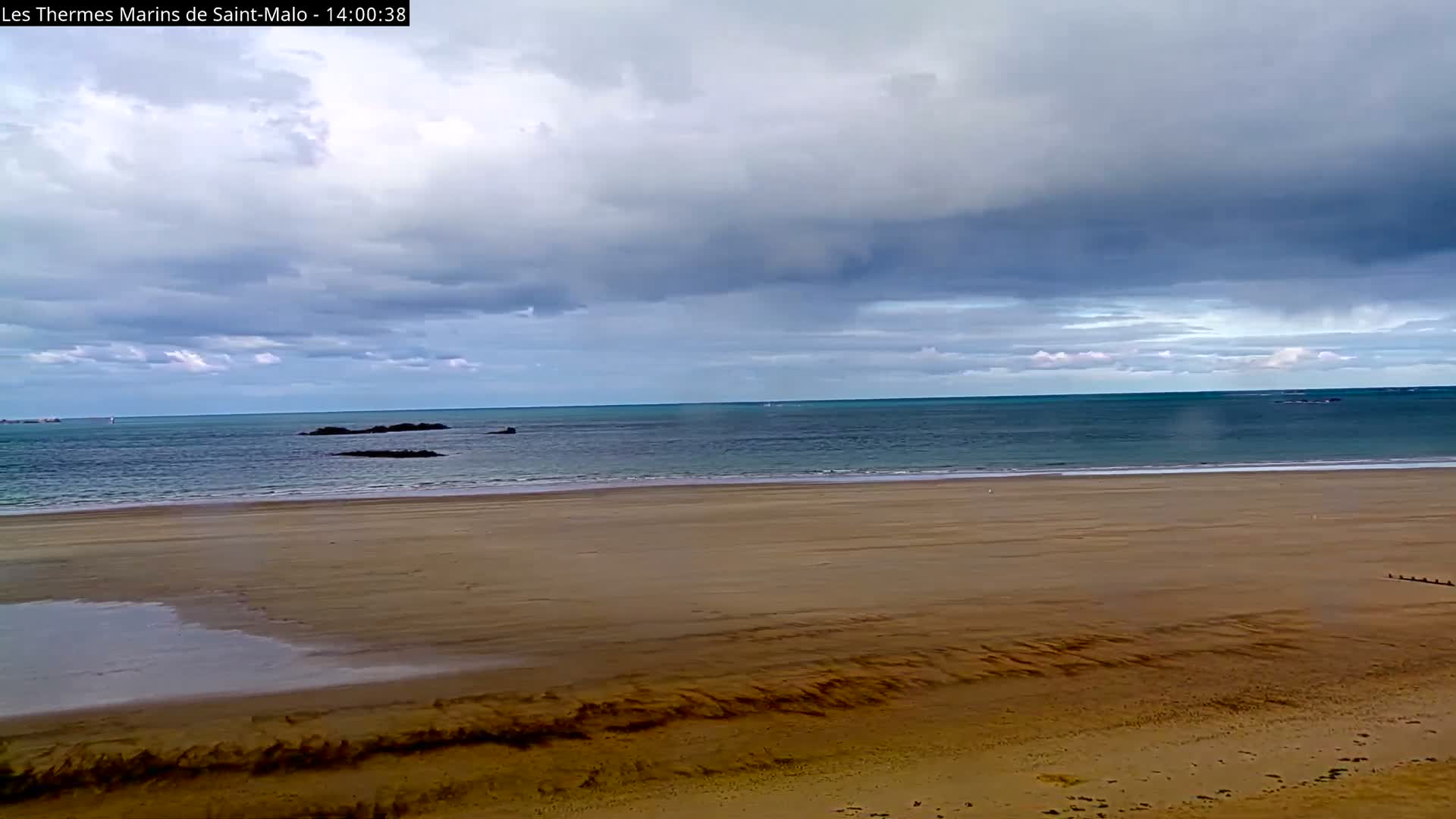 A stone fortress sits on a rocky outcropping in a calm, blue ocean under a mostly clear sky with a few scattered clouds.