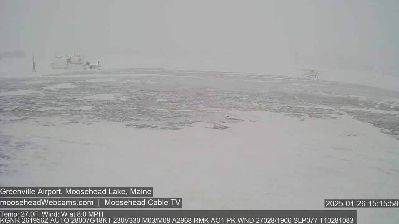 A snow-covered airfield is visible in heavy snow with low visibility.
