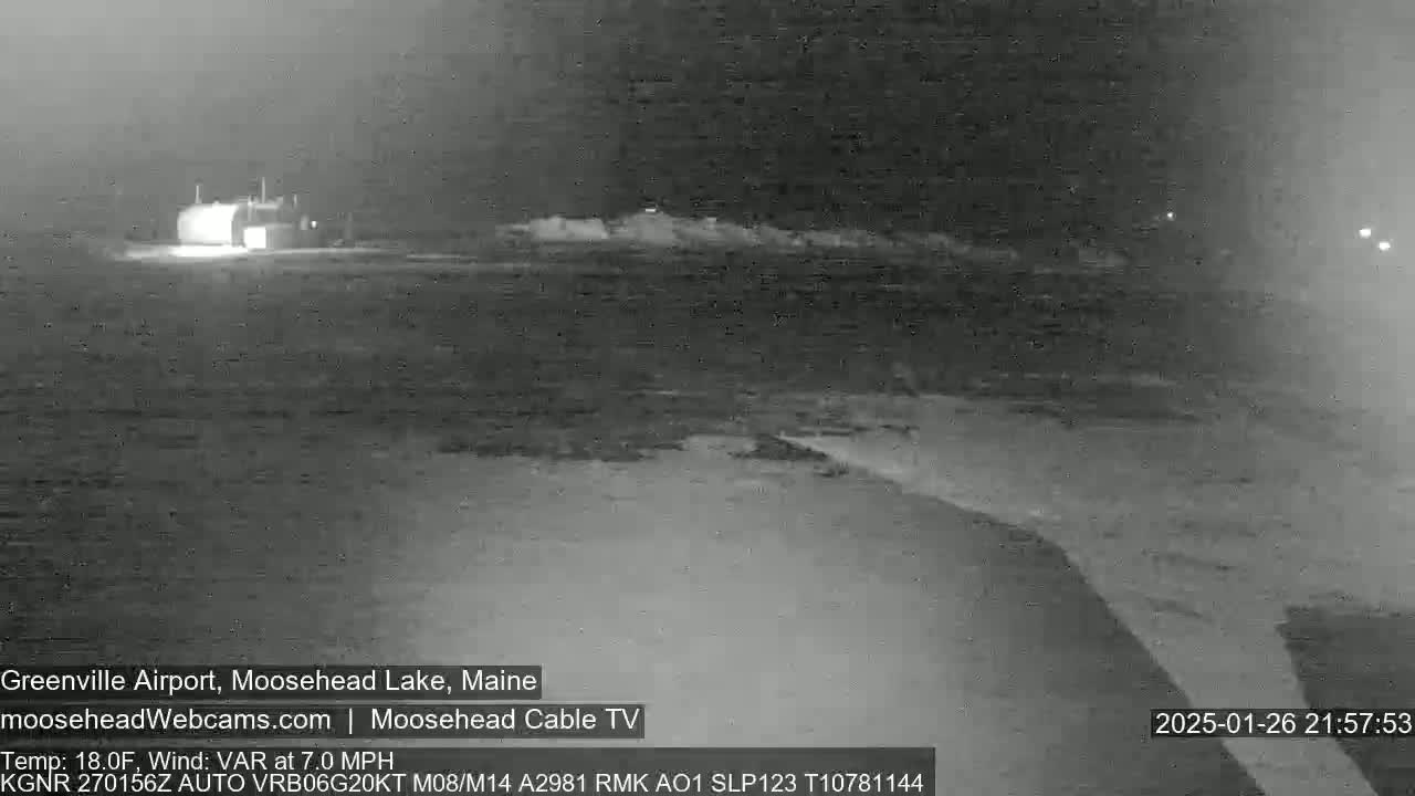A nighttime, low-light image shows a building and a flat, snow-covered landscape with variable wind at 7 mph and a temperature of 18 degrees Fahrenheit.