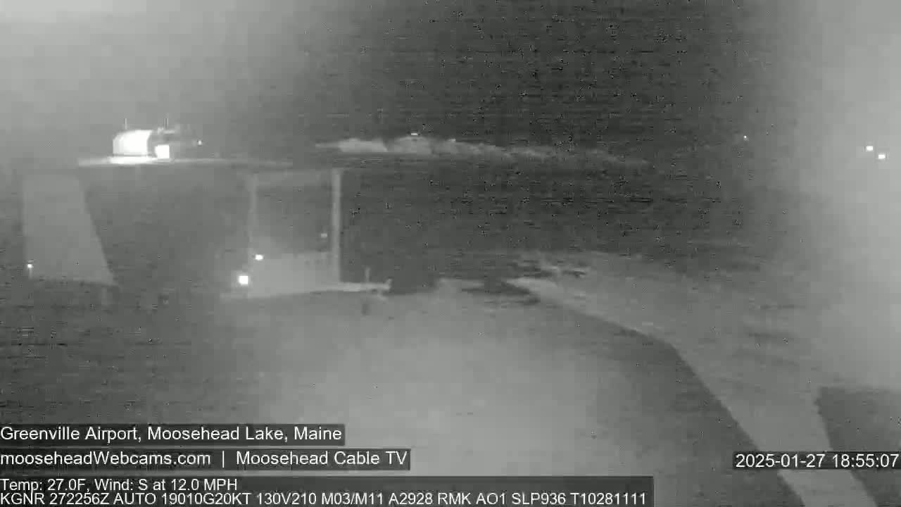 A nighttime, low-light view of a dark, snow-covered landscape with a building visible in the distance under a hazy sky, with a south wind at 12 mph and a temperature of 27°F.