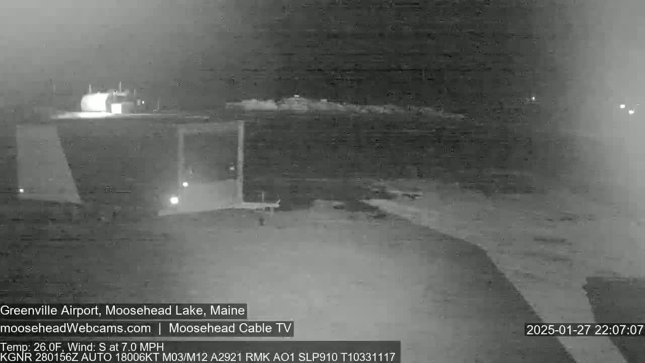 A nighttime, low-light view of a dark, snow-covered landscape shows a building in the distance under a cloudy sky with a south wind at 7.0 mph and a temperature of 26 degrees Fahrenheit.
