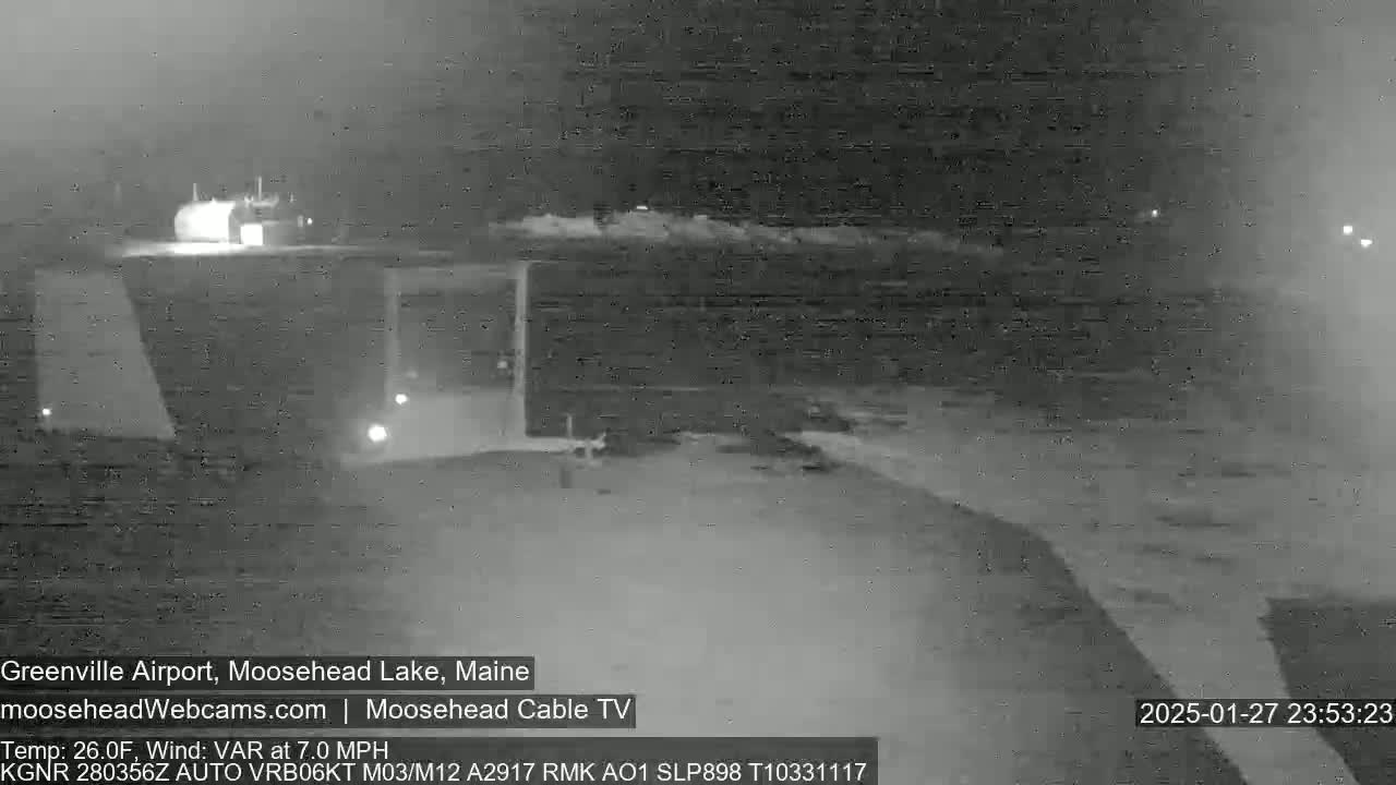 A nighttime, low-light view of a dark body of water near a building with a 7.0 mph variable wind and a temperature of 26 degrees Fahrenheit.