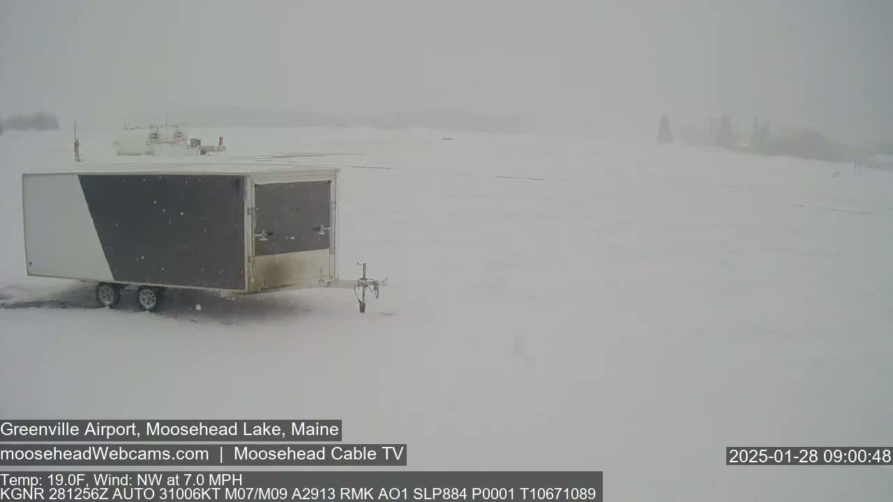 A gray and white enclosed trailer sits in a snow-covered area during a heavy snowstorm.