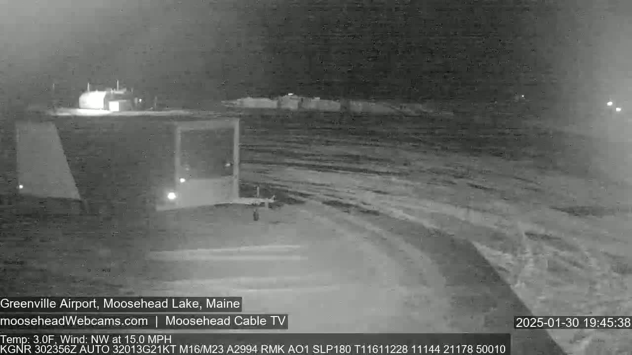 A nighttime, low-light view of a snow-covered road and a building, with a northwest wind at 15 mph and a temperature of 3 degrees Fahrenheit.