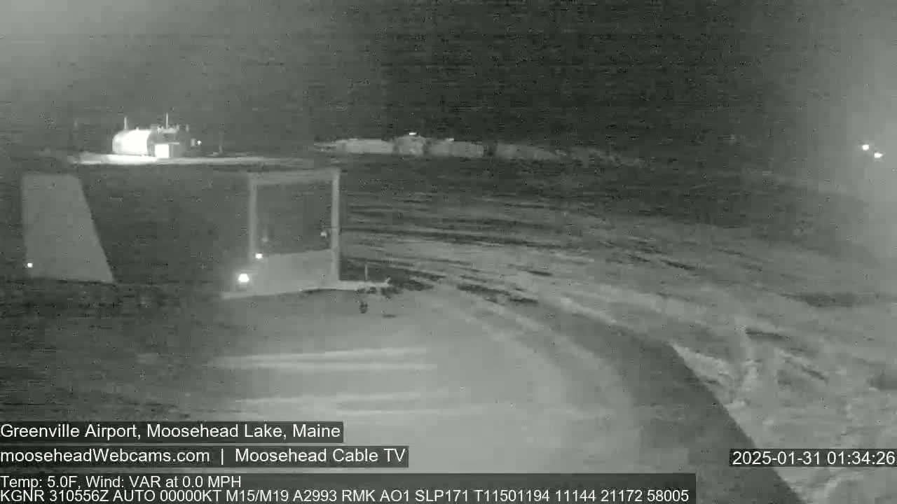 A nighttime, snow-covered airport scene is shown under dark, cloudy skies.