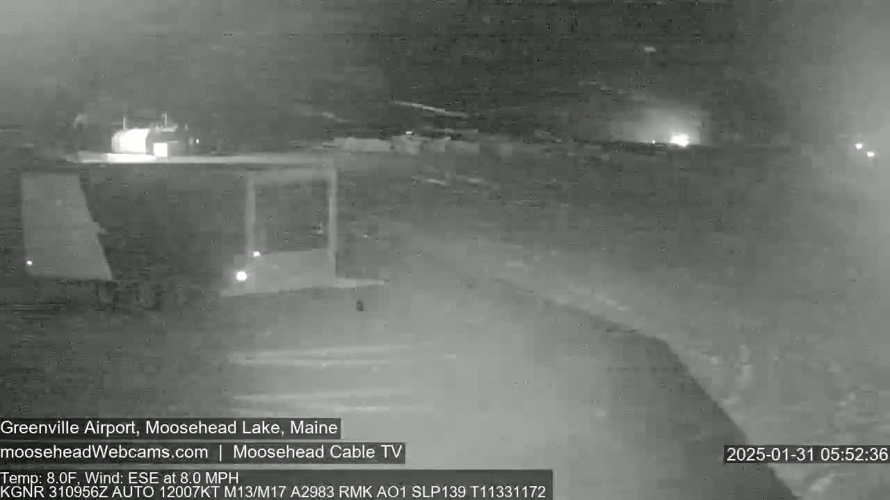 A nighttime, low-light view of an airport runway with a building in the background, under windy, eight-degree Fahrenheit conditions.