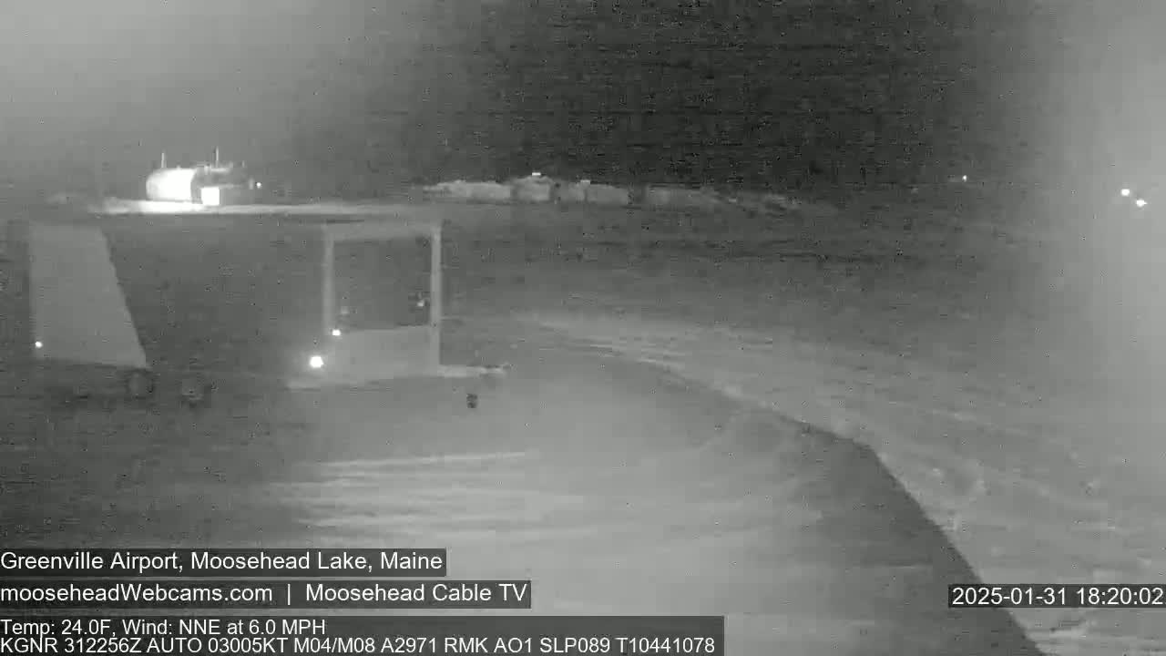 A nighttime, low-light view of a dark, possibly snowy, landscape near a building with a slight wind blowing from the north-northeast at 6.0 mph and a temperature of 24 degrees Fahrenheit.