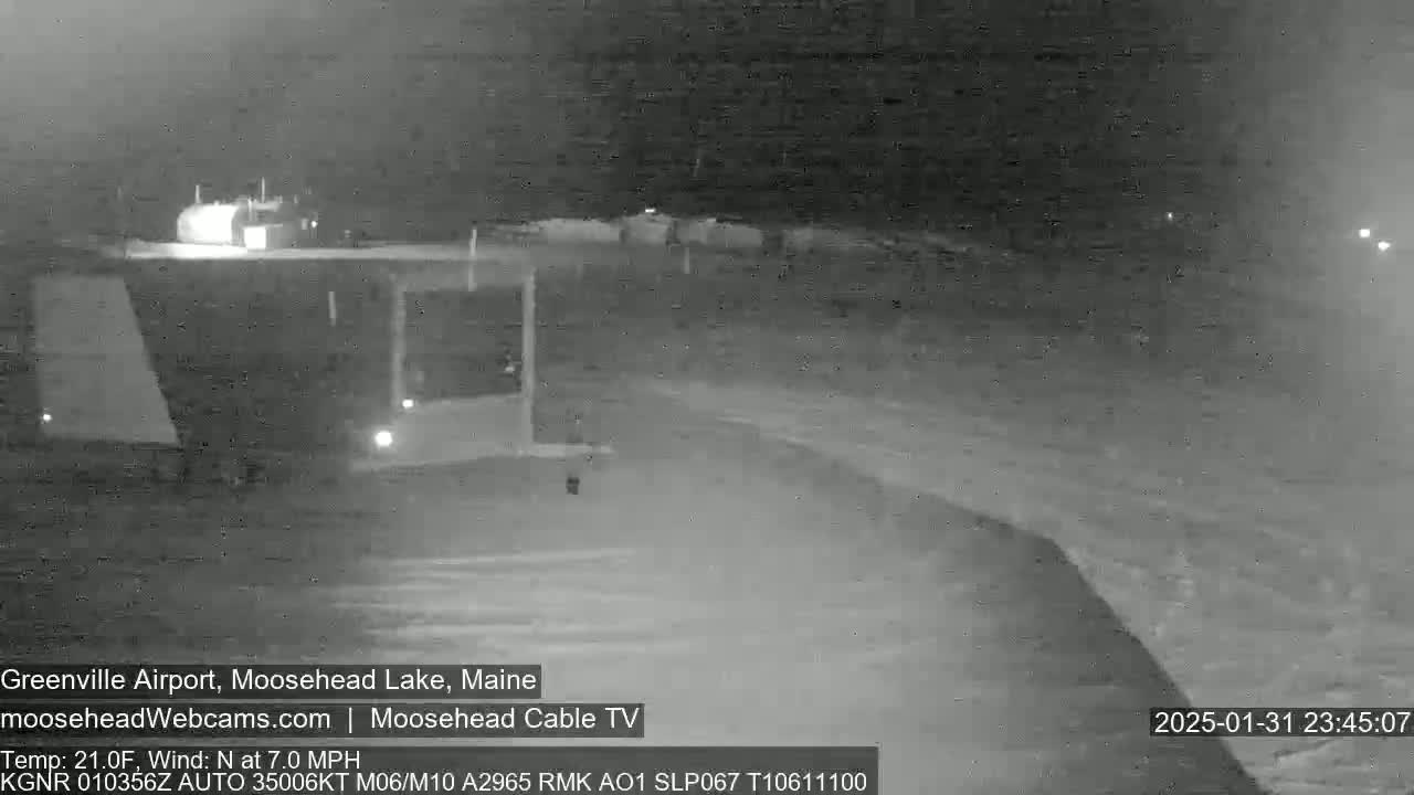 A nighttime, low-light grayscale image shows a mostly empty airport tarmac with a few vehicles visible under a dark sky.