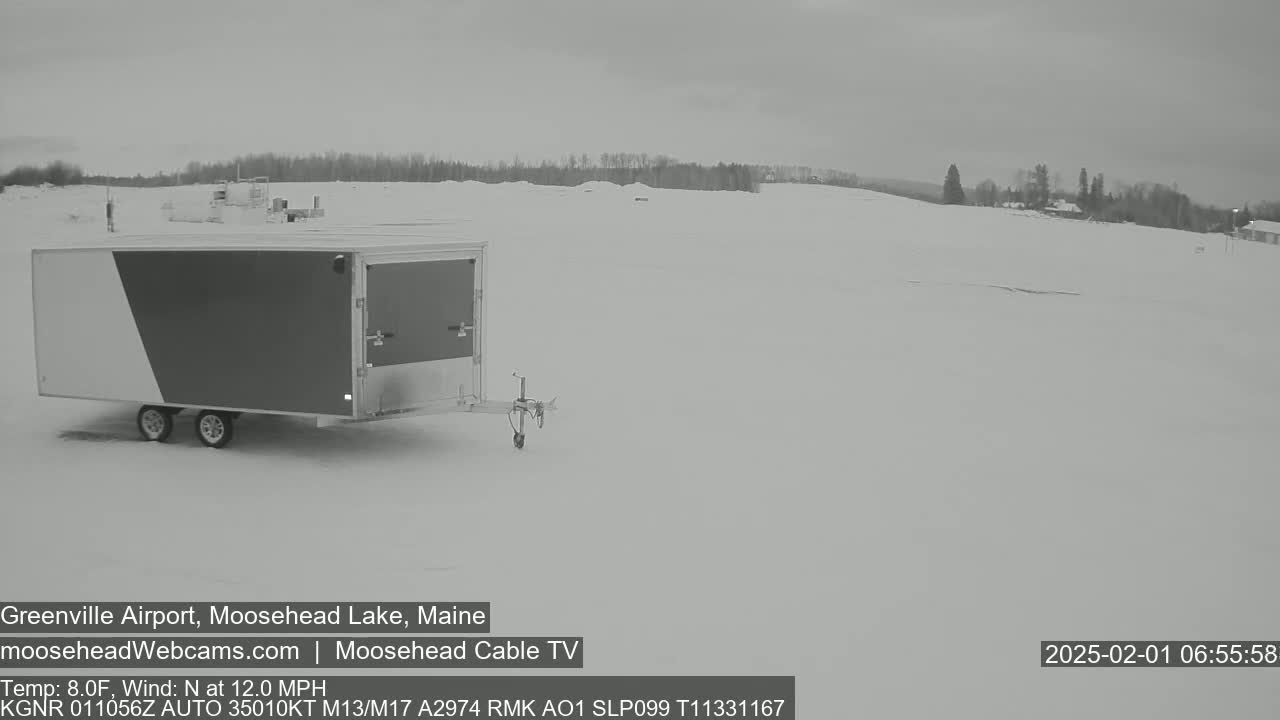 A large enclosed trailer sits in a snow-covered field under an overcast sky.