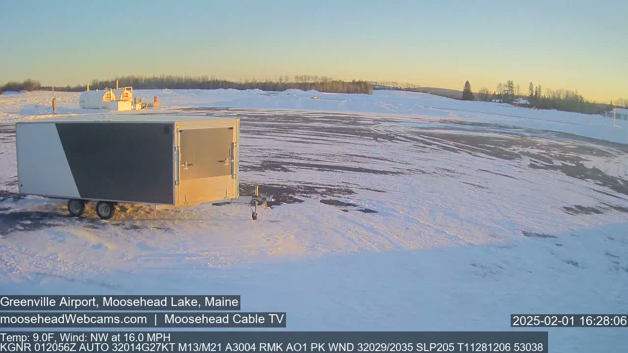 A gray and white enclosed trailer sits in a snowy airfield at sunset, with a  northwest wind blowing at 16 mph.