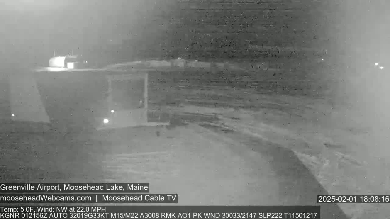 A nighttime, low-visibility view of a snow-covered airport runway with a building in the background, under a northwest wind of 22 mph and a temperature of 5°F.