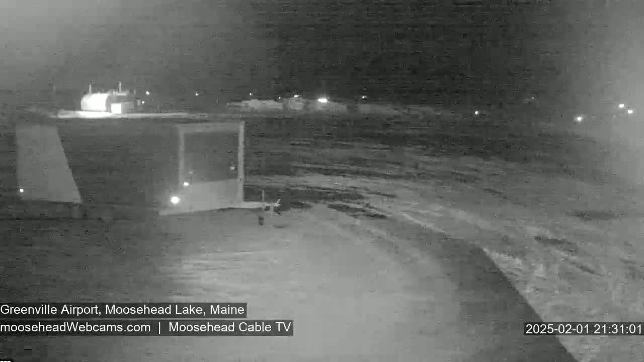 A nighttime, snowy scene shows a building and a snow-covered expanse of land.