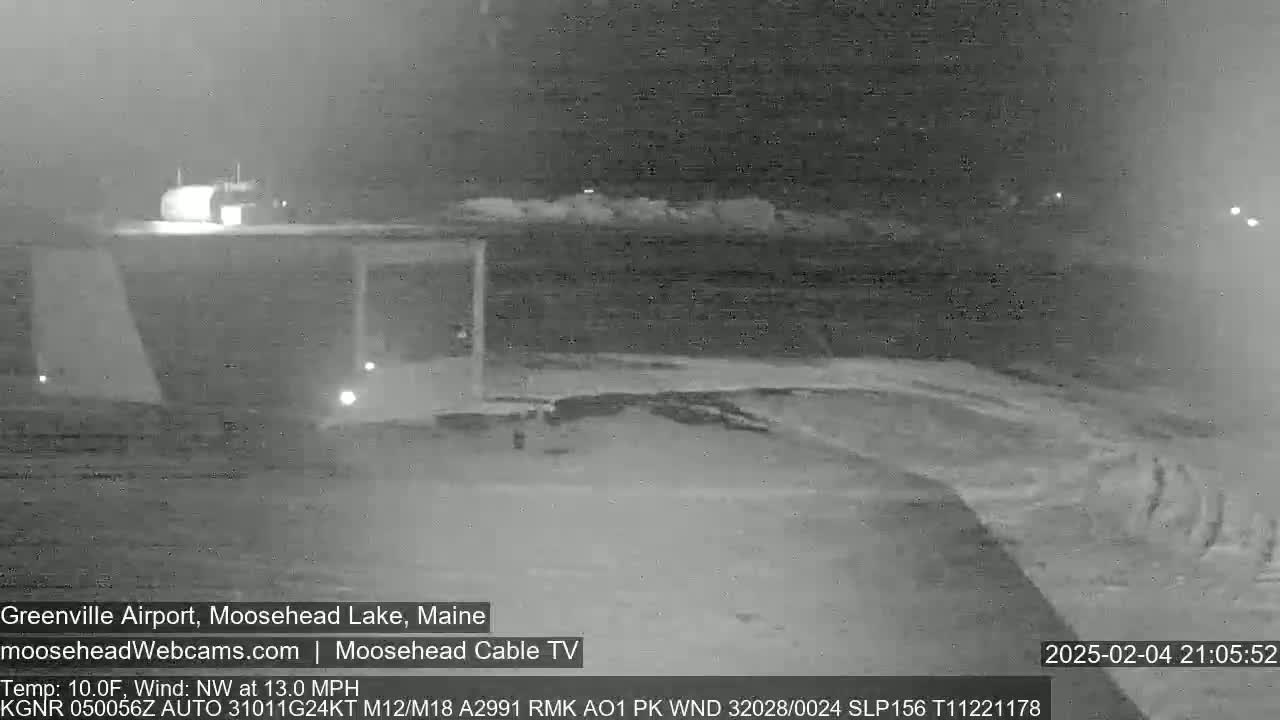 A nighttime, snow-covered scene shows a building and a road under a northwest wind blowing at 13 miles per hour with a temperature of 10 degrees Fahrenheit.