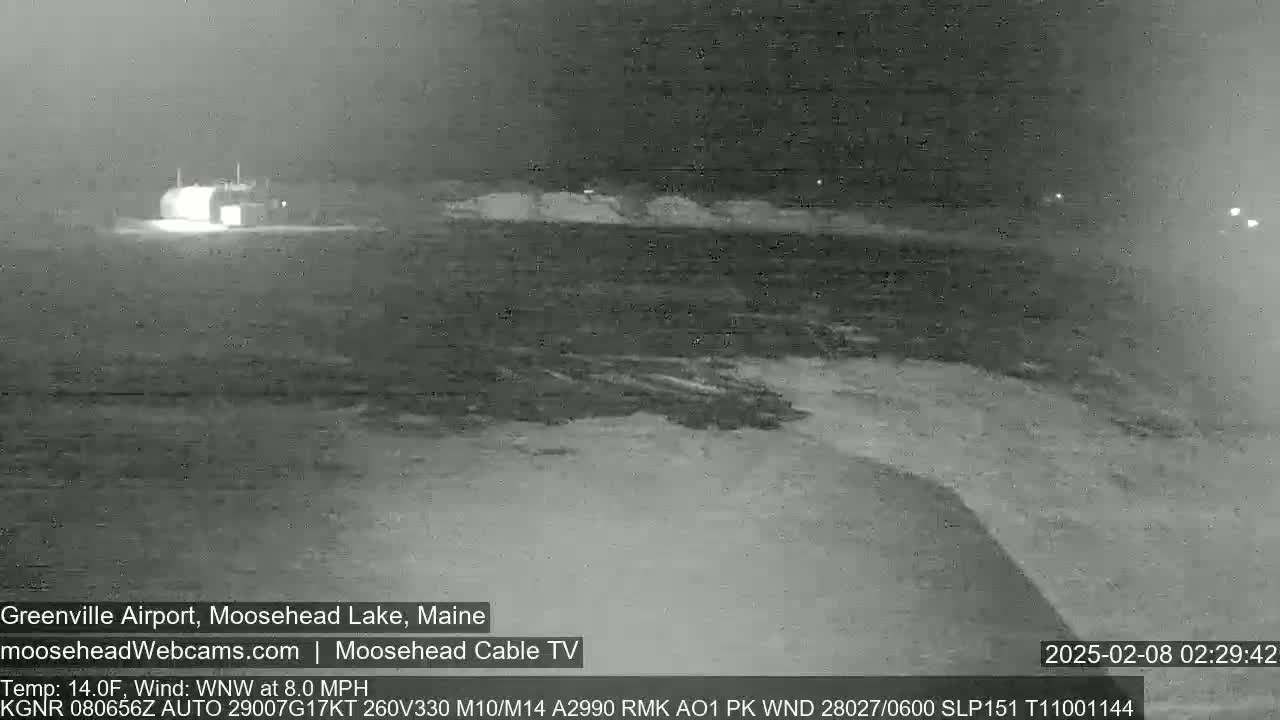 A nighttime, low-light image shows a building near a body of water under a dark, cloudy sky with a wind blowing from the west-northwest at 8 miles per hour and a temperature of 14 degrees Fahrenheit.