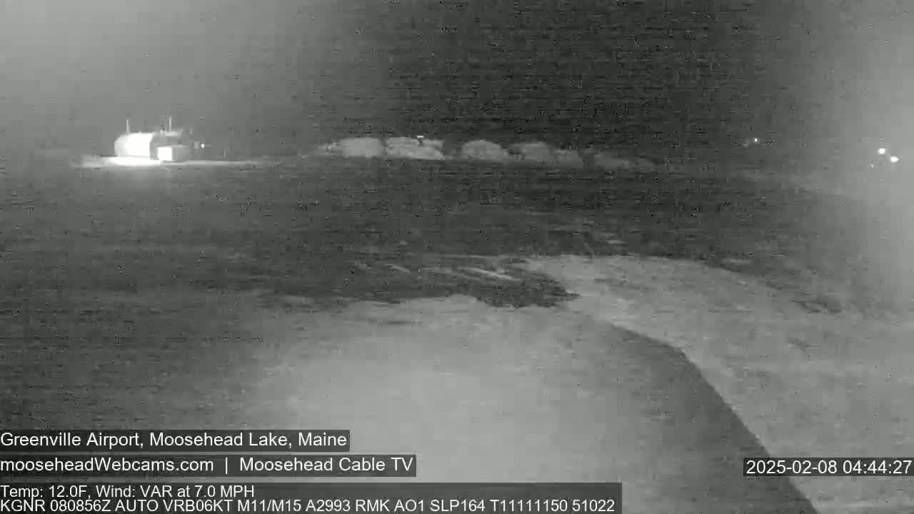 A nighttime, infrared view shows a mostly empty airport runway and a building in the distance under variable wind conditions and a temperature of 12 degrees Fahrenheit.