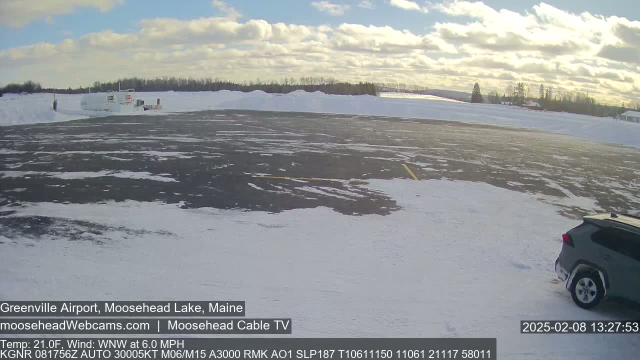 A mostly empty snow-covered tarmac with a dark-colored SUV parked near the bottom right, under a partly cloudy sky.