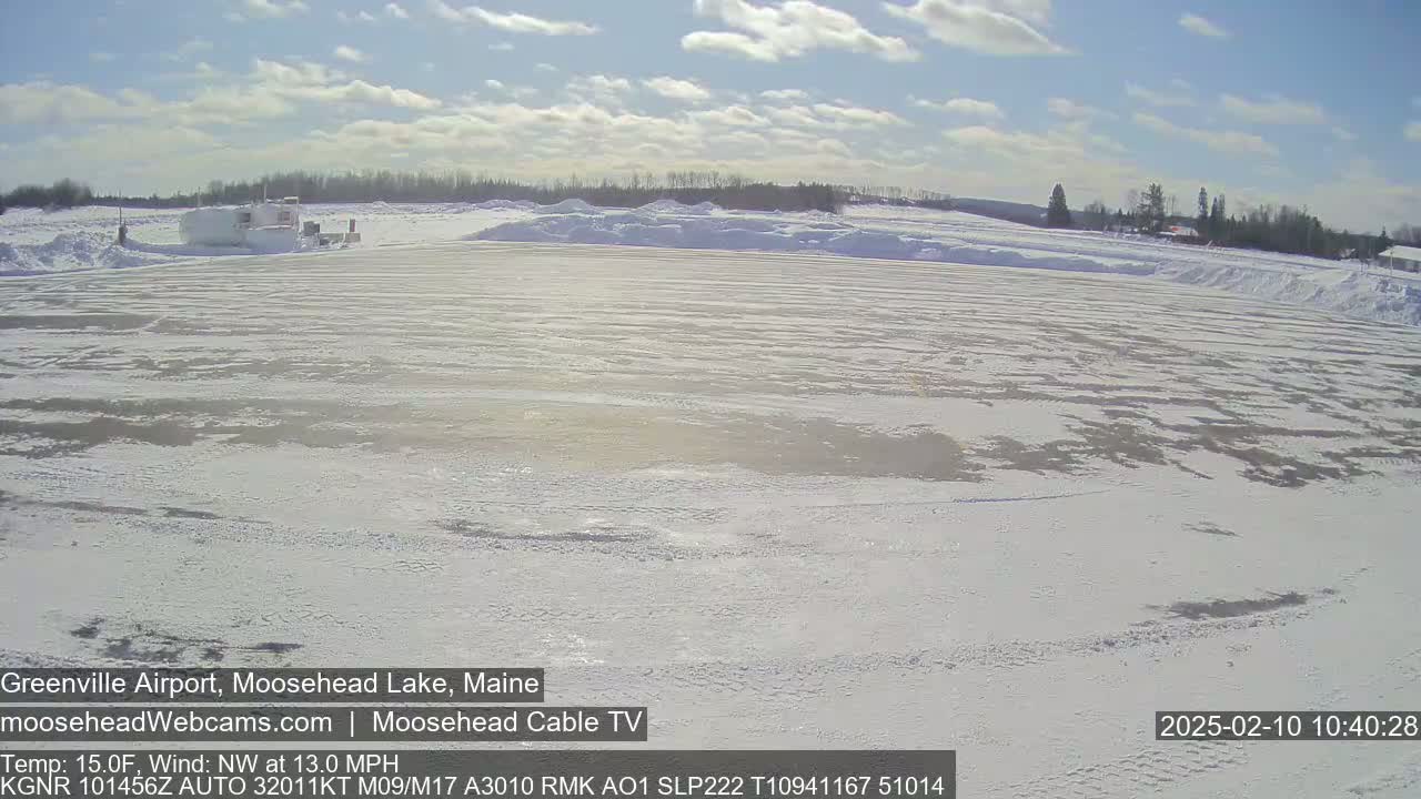 A snow-covered airfield with a building in the background under a partly sunny sky.